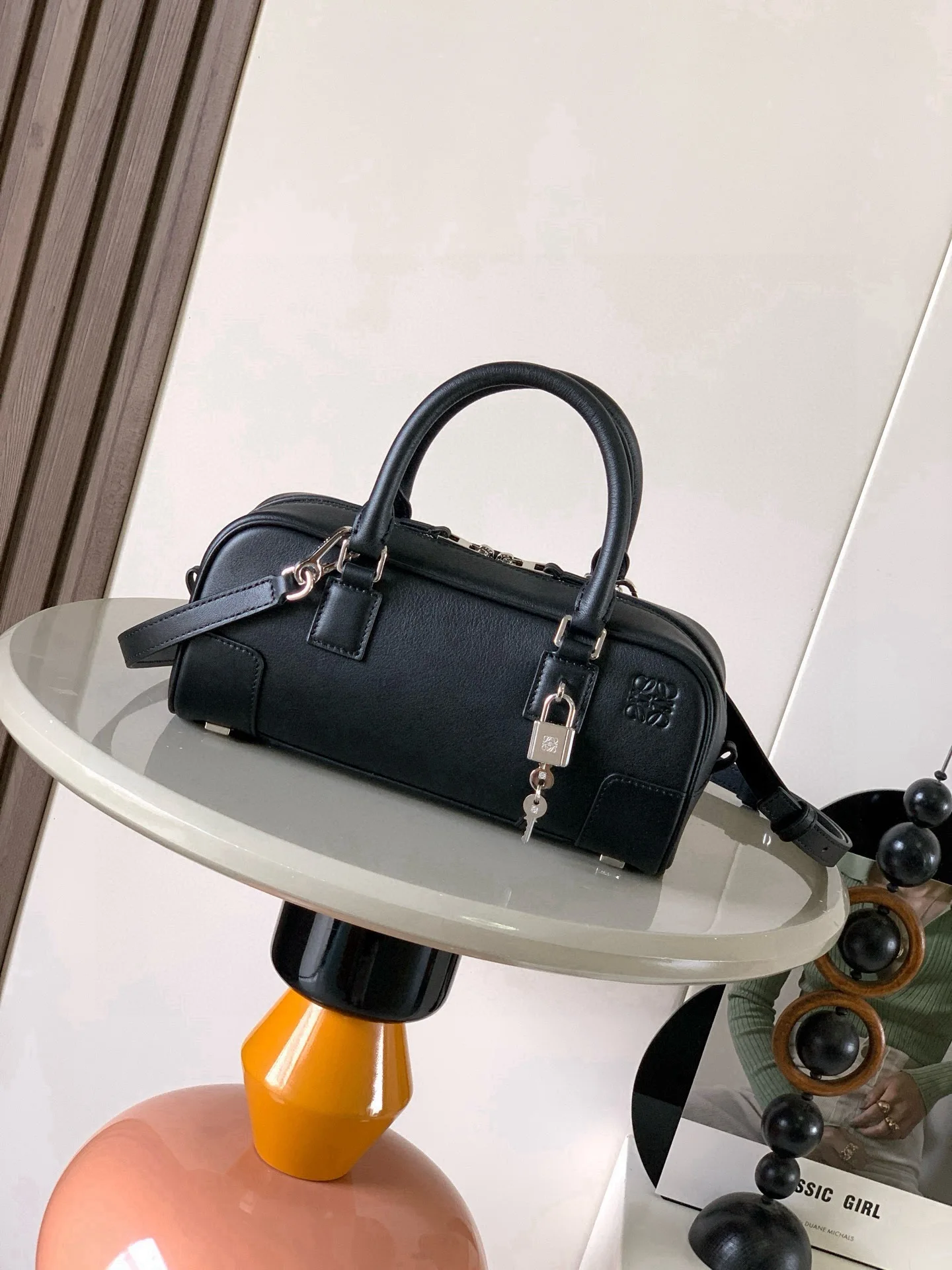 新款 明星同款手袋 Amazona 是 LOEWE 最初于1970年代推出的标志性手袋 采用精致比例和关键细节包括 Anagram 镌刻挂锁短款以纳帕牛皮革打造而成 可肩背 斜挎或手提 可拆卸可调节肩带 拉链开合 牛皮革拉链头 一个内部拉链隔层 一个插袋 一个挂锁钥匙收纳袋 包底以金属脚钉保护 金色绒面革衬里* Anagram 压纹尺寸 23cm 10cm 11cm款号 9085颜色 黑色银锁