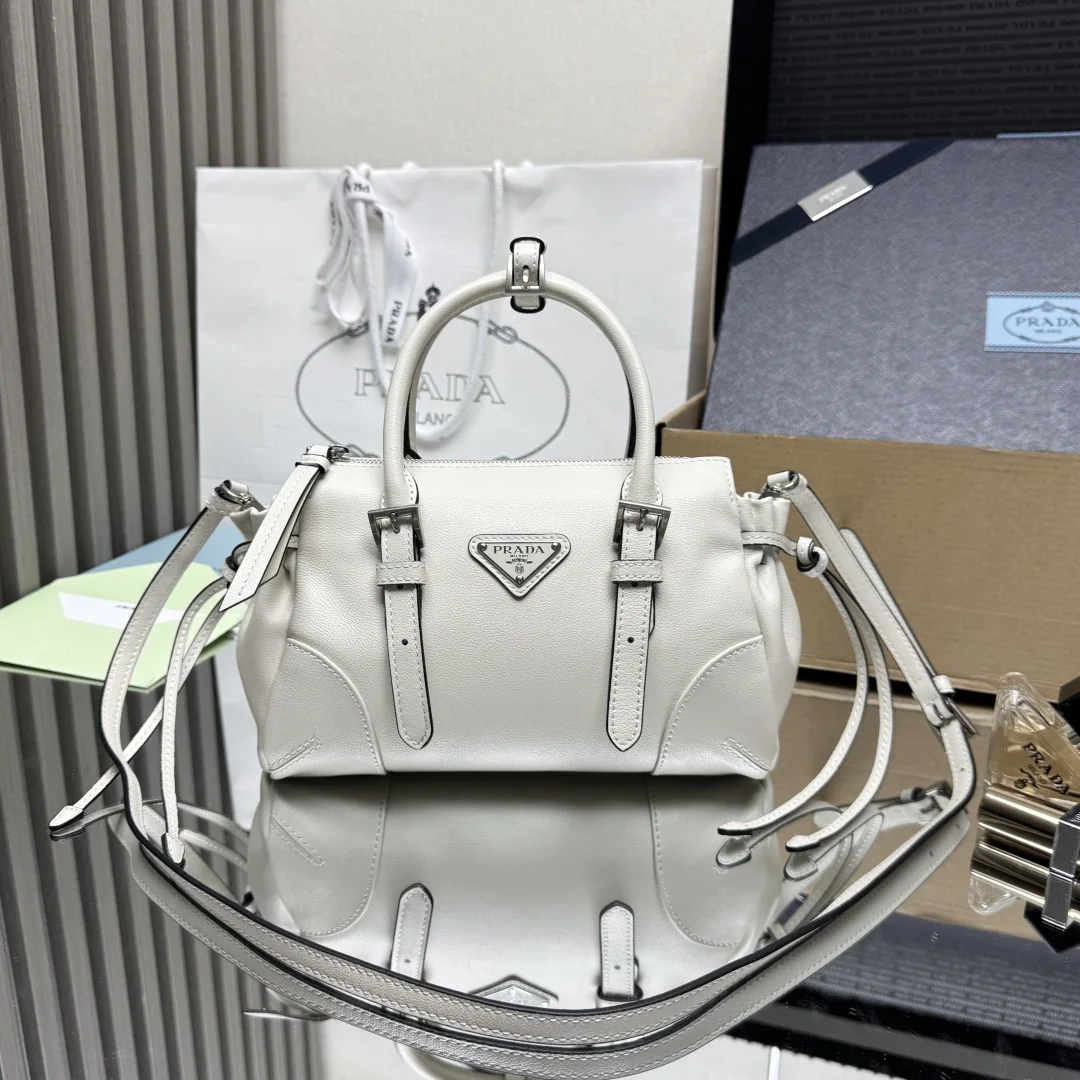 原单普拉达女包|高仿普拉达女包|精仿普拉达女包|一比一普拉达女包 顶级原单 新品1BA499迷你这款迷你Bonnie呈现利落而随性的大都会风格 柔和廓形融入侧面系带与金属搭扣等标志性细节 包身结构紧凑 配有一条可拆卸长肩带 可手提亦可配合肩带背携 容量空间大 又是一款永久不过时爆款尺寸 长24x高14x底9cm