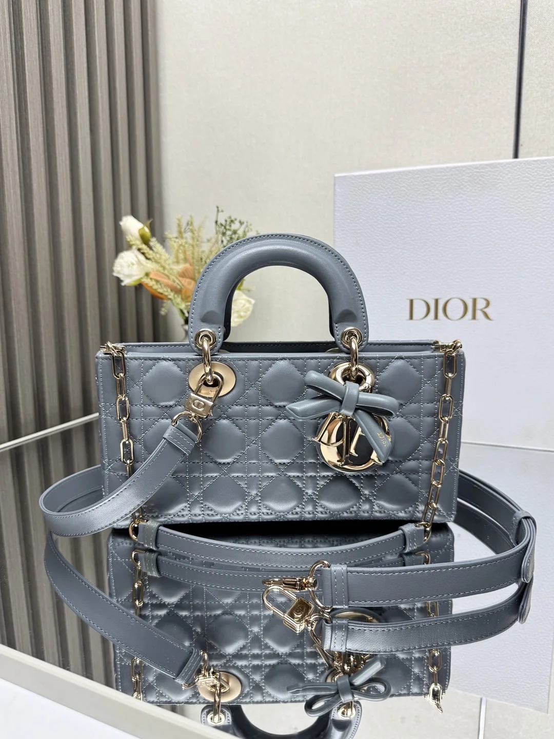 中号 LADY D-JOY 手袋 雾霾蓝带蝴蝶结小羊皮 这款 Lady D-Joy 手袋凸显 Lady Dior 系列的简约美学 集中体现了 Dior 对典雅和美丽的深刻洞见 采用黑色哑光牛皮革精心制作 以经典的藤格纹缉面线打造醒目的绗缝细节 精良的缝制工艺显露无遗 同色调金属 D.I.O.R. 吊饰彰显优雅气质 小号款式 搭配可拆卸的链条肩带和可调节 可拆卸的皮革肩带 可手提 肩背或斜挎 是日常造型的理想之选 可拆卸链条肩带可拆卸 可调节的皮革肩带型号 0540尺寸 26×13.5×5 cm可收纳一部 iPhone和其他配饰238620