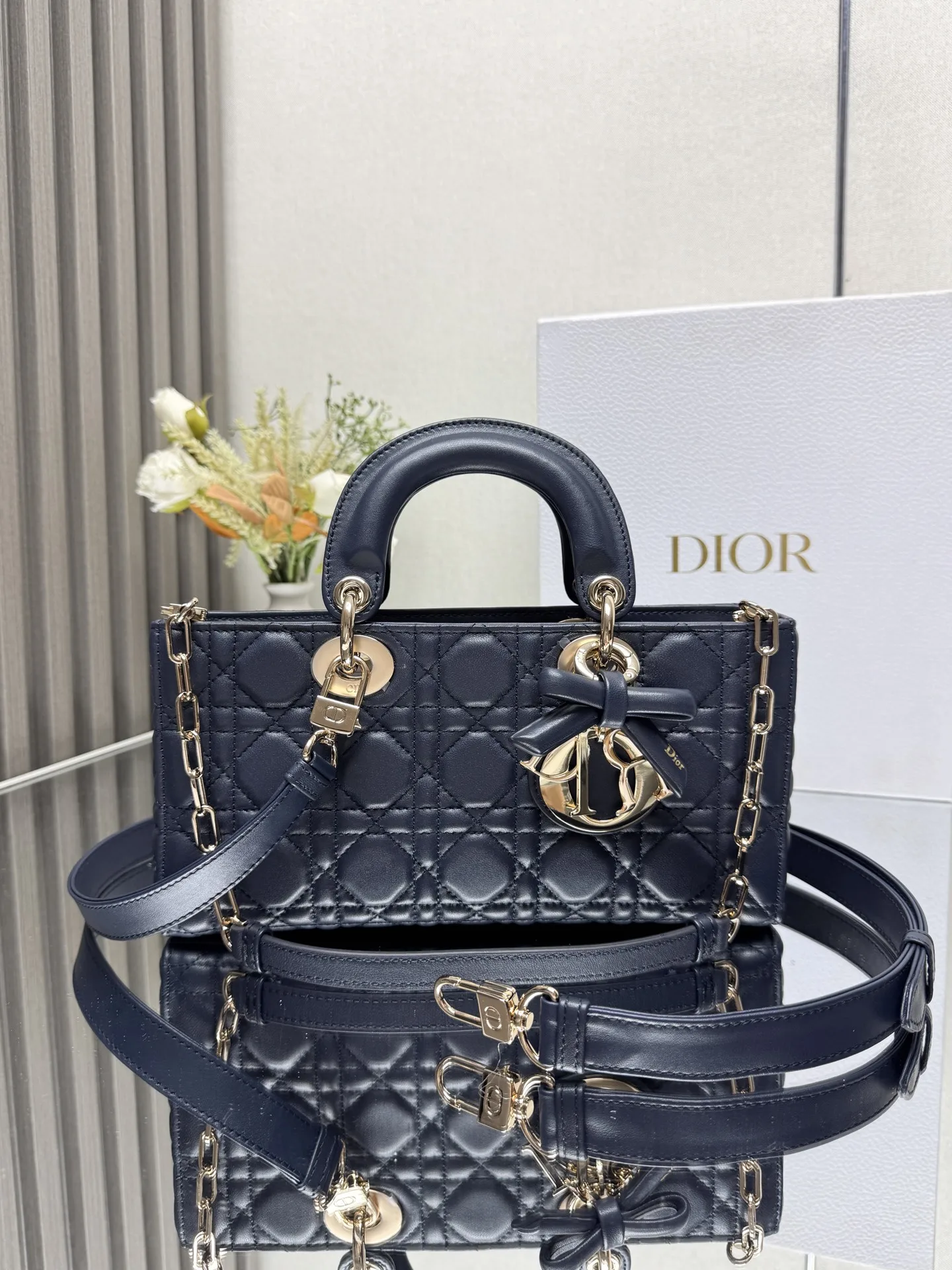 中号 LADY D-JOY 手袋 深蓝色带蝴蝶结小羊皮 这款 Lady D-Joy 手袋凸显 Lady Dior 系列的简约美学 集中体现了 Dior 对典雅和美丽的深刻洞见 采用黑色哑光牛皮革精心制作 以经典的藤格纹缉面线打造醒目的绗缝细节 精良的缝制工艺显露无遗 同色调金属 D.I.O.R. 吊饰彰显优雅气质 小号款式 搭配可拆卸的链条肩带和可调节 可拆卸的皮革肩带 可手提 肩背或斜挎 是日常造型的理想之选 可拆卸链条肩带可拆卸 可调节的皮革肩带型号 0540尺寸 26×13.5×5 cm可收纳一部 iPhone和其他配饰238620