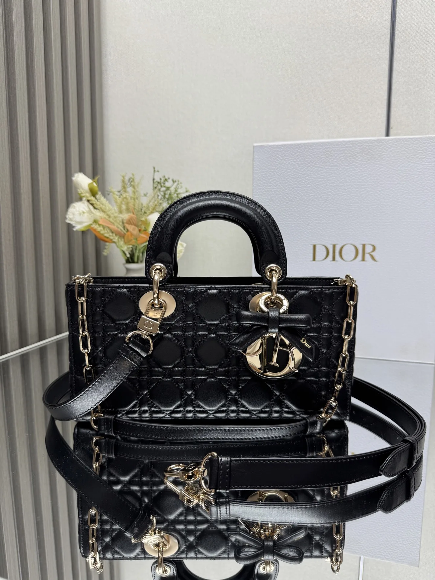 中号 LADY D-JOY 手袋 黑色带蝴蝶结小羊皮 这款 Lady D-Joy 手袋凸显 Lady Dior 系列的简约美学 集中体现了 Dior 对典雅和美丽的深刻洞见 采用黑色哑光牛皮革精心制作 以经典的藤格纹缉面线打造醒目的绗缝细节 精良的缝制工艺显露无遗 同色调金属 D.I.O.R. 吊饰彰显优雅气质 小号款式 搭配可拆卸的链条肩带和可调节 可拆卸的皮革肩带 可手提 肩背或斜挎 是日常造型的理想之选 可拆卸链条肩带可拆卸 可调节的皮革肩带型号 0540尺寸 26×13.5×5 cm可收纳一部 iPhone和其他配饰238620